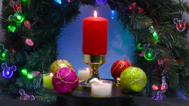 一支由彩球和小蜡烛环绕的燃烧的蜡烛在圣诞花圈和照明的背景下旋转着 — 图库视频影像