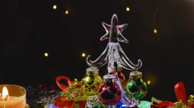 Bir desenli yüzeyde, Noel çanları ve küçük mumlarla çevrili küçük bir Noel ağacı.