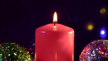Büyük bir mum, Noel topları ve küçük mumlarla çevrili desenli bir yüzey üzerinde döner.