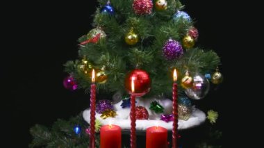 Noel armut ve Noel ağacı dalları olan beyaz bir battaniyenin üzerinde dönen bir Noel ağacının yanan mumlarının arkasında hareket halindedir.