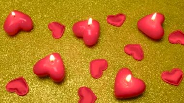 Parlak altın bir yüzeyde yanan bir sürü mum ve kalp var.