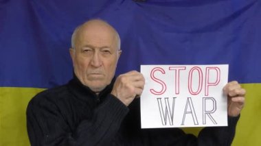 Ukrayna bayrağının arka planında duran yaşlı bir adam, bir Savaş Durdurma işareti kaldırdı.
