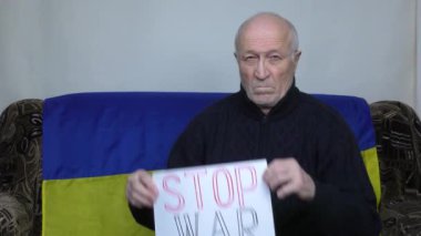 Ukrayna bayrağının arka planında yaşlı bir adam Savaş Durdurma işaretini kaldırıyor.