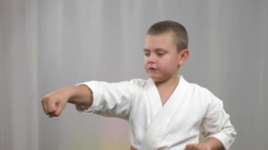 Turuncu kuşaklı küçük bir karategi sporcusu hafif bir arka planda yumrukları yener.