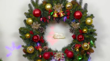 Büyük bir Noel çelengi yanan mumların ve vazoların arkasında asılı.