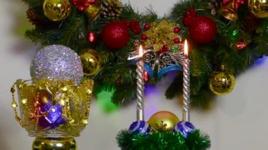 Two burning candles near a ball in a vase and a rotating Christmas tree