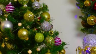 Noel 'de yanıp sönen sarı ışıkları olan bir Noel ağacı elinde top ve Noel çelengi olan bir vazonun yanında döner.