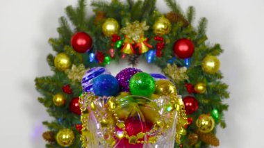 Bir Noel çelenginin arka planında, ortasında Noel topları olan bir vazo dönüyor.