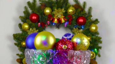 Bir Noel çelenginin arka planında ortasında çok renkli büyük toplar olan bir vazo dönüyor.