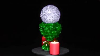 Bir Noel balosu, yeşil bir stantta yanan iki kırmızı mum arasında döner.