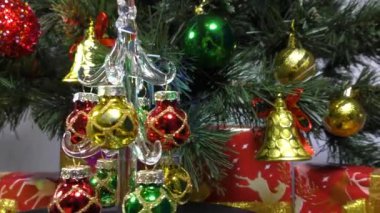 A small Christmas tree is spinning against the background of a green Christmas tree and gifts