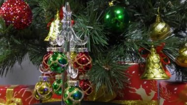A small Christmas tree slowly spins against the background of a green Christmas tree and gifts