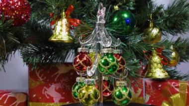 Video postcard a small Christmas tree slowly spins against the background of a green Christmas tree and gifts