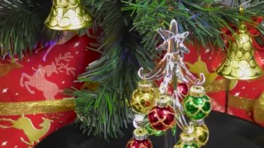 Close-up of a small Christmas tree rotates on the background of a green Christmas tree and gifts