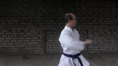 The athlete performs punches and blocks with his hands on a brick wall background