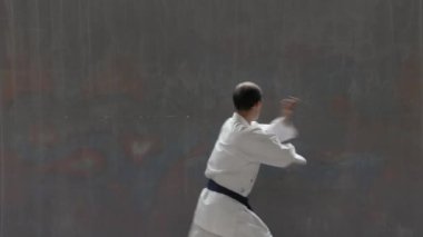 Young sportsman with blue belt performs formal exercises against street wall background