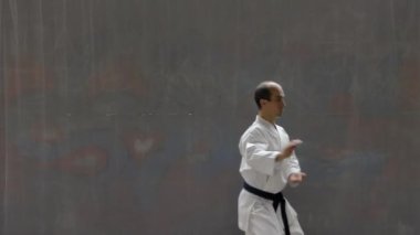 Young sportsman with blue belt performs formal exercises against the background of a street wall
