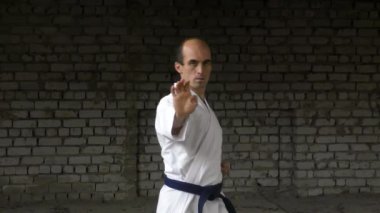 Against the background of a brick wall, an athlete trains punches and blocks with his hands