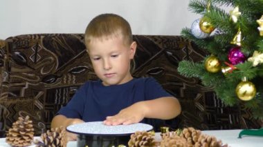 A little boy puts Christmas decorations on a spinning stand