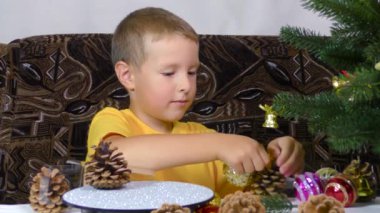 A little boy is playing with Christmas decorations near the Christmas tree