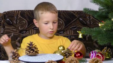 A little boy is playing with Christmas decorations near the Christmas tree