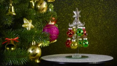 On a colored background, a small Christmas tree rotates near a beautiful decorated Christmas tree