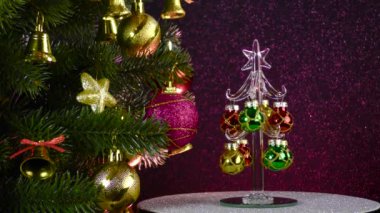 On a colored background, a small Christmas tree rotates near a beautiful decorated Christmas tree