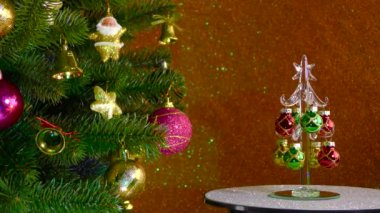 On a colored background, a small Christmas tree rotates near a beautiful decorated Christmas tree