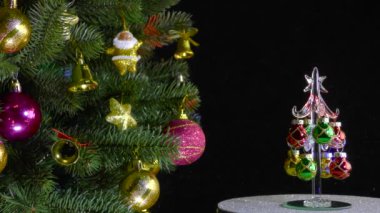 On a black background, a small Christmas tree rotates near a beautiful decorated Christmas tree