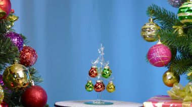 On a blue background, a small Christmas tree rotates near large Christmas trees decorated with Christmas decorations