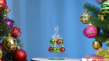 On a blue background, a small Christmas tree rotates near large Christmas trees decorated with Christmas decorations