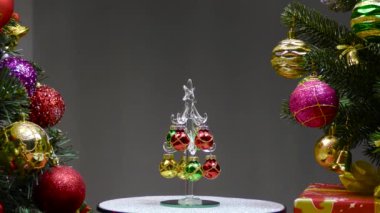 On a gray background, a small Christmas tree rotates near large Christmas trees decorated with Christmas decorations