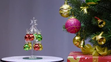 On a gray background, a small Christmas tree rotates near a large Christmas tree decorated with Christmas decorations