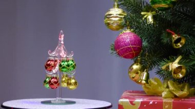 On a gray background, a small Christmas tree rotates near a large Christmas tree decorated with Christmas decorations