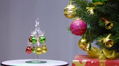 On a gray background, a small Christmas tree rotates near a large Christmas tree decorated with Christmas decorations