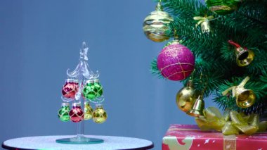 On a blue background, a small Christmas tree rotates near a large Christmas tree decorated with Christmas decorations.