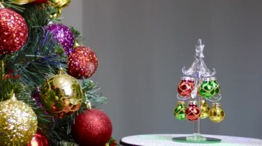 On a gray background, a small Christmas tree rotates near a large Christmas tree decorated with Christmas decorations