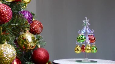 On a gray background, a small Christmas tree rotates near a large Christmas tree decorated with Christmas decorations