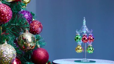 On a blue background, a small Christmas tree rotates near a large Christmas tree decorated with Christmas decorations.