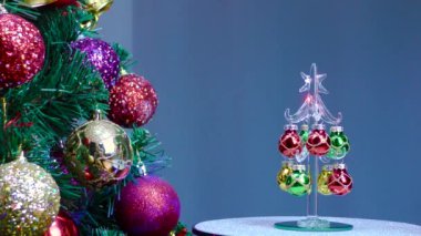 On a blue background, a small Christmas tree rotates near a large Christmas tree decorated with Christmas decorations.