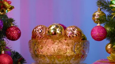 On a colored background, a vase with Christmas balls rotates near a large Christmas tree decorated with Christmas decorations