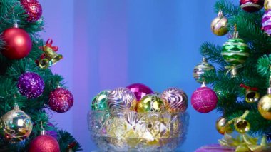 On a colored background, a vase with Christmas balls rotates near a large Christmas tree decorated with Christmas decorations