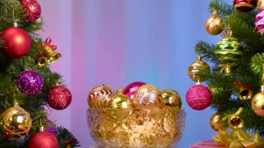 On a colored background, a vase with Christmas balls rotates near a large Christmas tree decorated with Christmas decorations