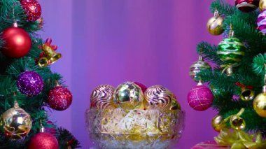 On a colored background, a vase with Christmas balls rotates near a large Christmas tree decorated with Christmas decorations