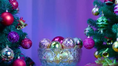 On a colored background, a vase with Christmas balls rotates near a large Christmas tree decorated with Christmas decorations