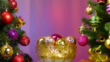 On a colored background, a vase with Christmas balls rotates near a large Christmas tree decorated with Christmas decorations