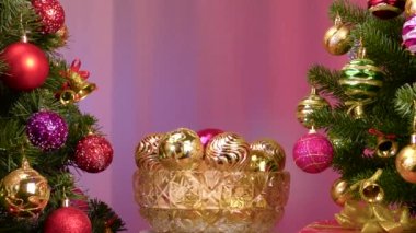 On a colored background, a vase with Christmas balls rotates near a large Christmas tree decorated with Christmas decorations