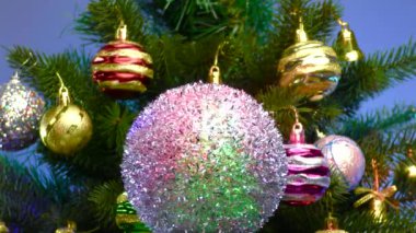 On a colored background, the Christmas ball rotates near a large Christmas tree decorated with Christmas decorations