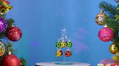 On a blue background, a small Christmas tree rotates near large Christmas trees decorated with Christmas decorations