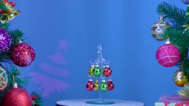 On a blue background, a small Christmas tree rotates near large Christmas trees decorated with Christmas decorations